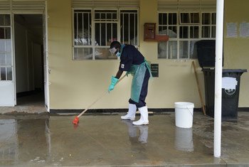 Funcionário de um centro de saúde em Uganda limpa o chão usando uma mistura de cloro e água para prevenir infecções. Serviços adequados de água, saneamento e higiene nas instalações de saúde são vitais para proteger as populações contra infecções.