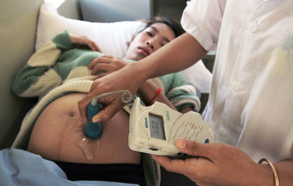 Uma mulher grávida recebe um ultra-som em uma cama de hospital, com um profissional de saúde usando um monitor de frequência cardíaca fetal EDAN.