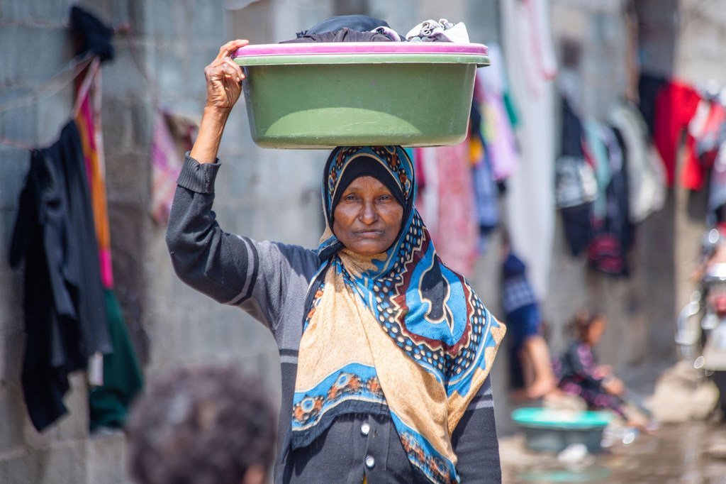 Une femme porte un bol avec des vêtements lavés dans un camp de personnes déplacées dans le district d'Al-Dhihar, au Yémen.