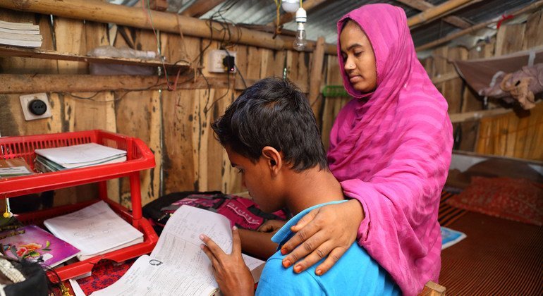 बांग्लादेश के जैसोर में पढ़ाई करता एक किशोर लड़का, साथ में उसकी माँ भी खड़ी है.