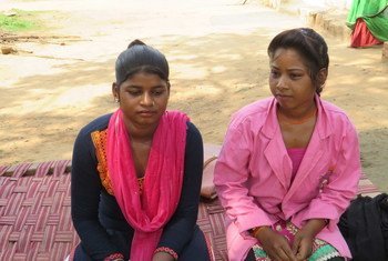भारत में दो युवतियां, लाली आदिवासी और रामकली आदिवासी, बाहर एक बुनी हुई चटाई पर बैठी हैं।