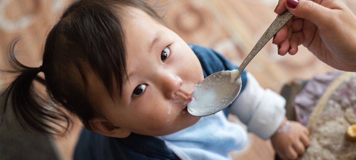 Ulaanbaatar, Mongolia - September 07, 2018: Mother giving porridge mixed with micronutrient powders (MNP) to her one-year old son in their house, in Ulaanbaatar, Mongolia. MNP aim to improve the quality of diets of nutritionally vulnerable groups, such as