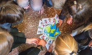 Niños en Ucrania juegan con un poster de los Objetivos de Desarrollo Sostenible que ilustran las diferentes razas alrededor del mundo.