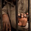 A fourteen-year-old migrant from Niger rests his hand on a gate inside a detention centre, in Libya.