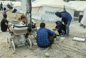 ग्रीस के लेसवॉस द्वीप स्थित मोरिया शिविर के आग में तबाह हो जाने के बाद, शरणार्थी एक अस्थाई स्थल पर खाना बकाते हुए और अपने मोबाइल चार्ज करते हुए.