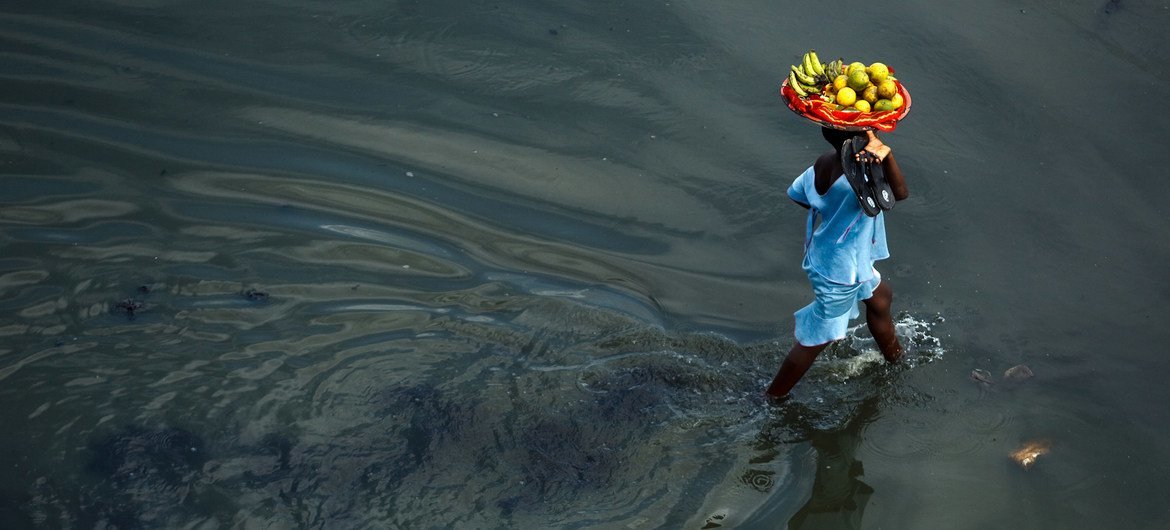 贝宁港口城市科托努，一个女孩头顶一篮水果走过洪水泛滥的街道。