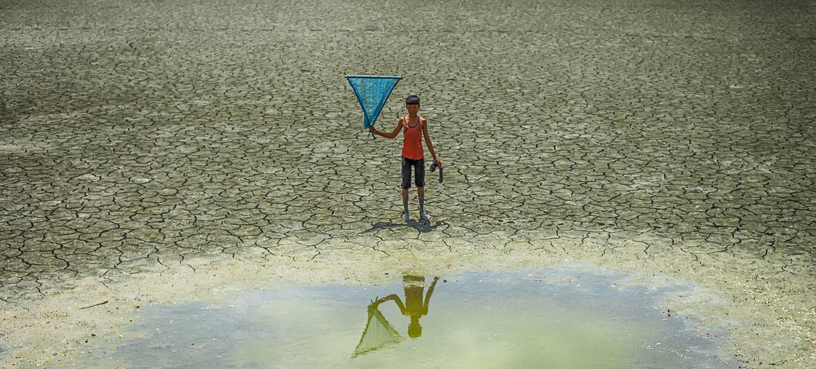 一个小男孩站在孟加拉国干旱地区的一个水坑前。