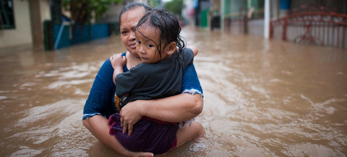 इण्डोनेशिया के जकार्ता में, एक महिला बाढ़ के दौरान अपनी बेटी के साथ रास्ता तय करते हुए