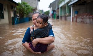 Mulher carrega a filha durante enchentes em Jacarta, Indonésia. 