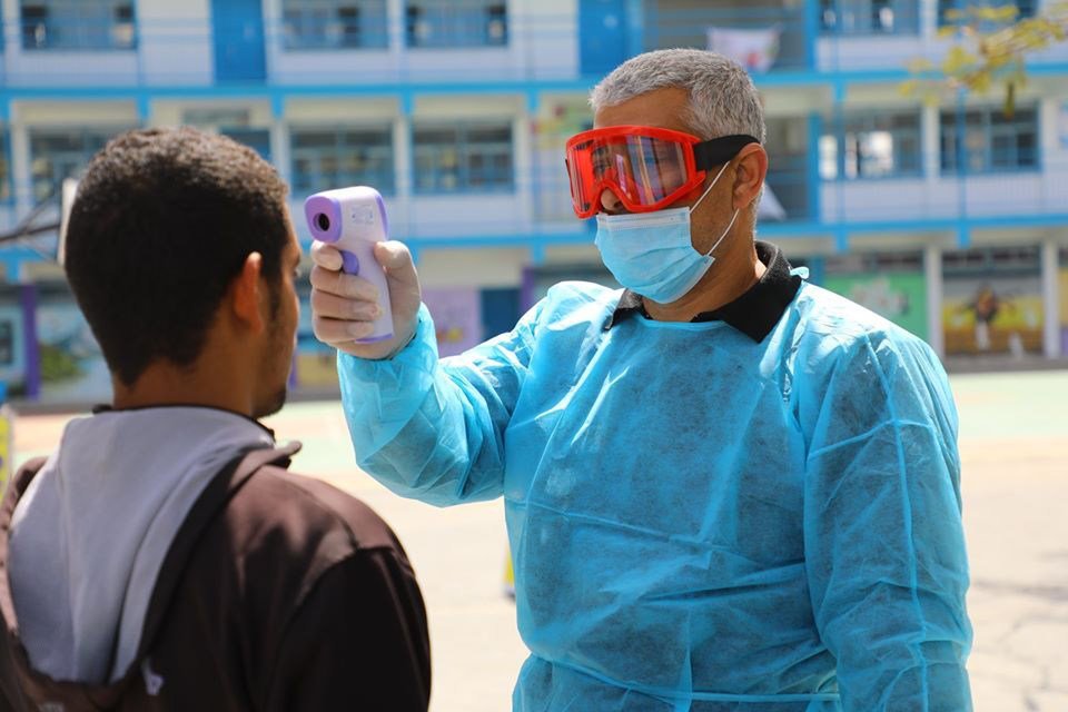 联合国近东救济工程处的工作人员在加沙的一所学校门前为学生测量体温。