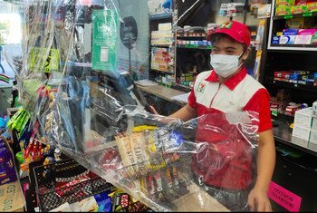 A convenience store requires staff to wear a mask, observe physical distance, and use a plastic sheet barrier as safety measures to prevent the spread of COVID-19, Muntinlupa City, Philippines.
