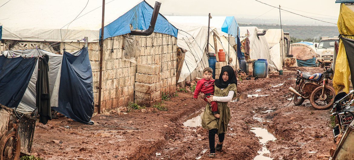 فتاة تسير في وحل وهي تحمل أخاها الصغير في مخيم خير الشام في محافظة إدلب السورية.