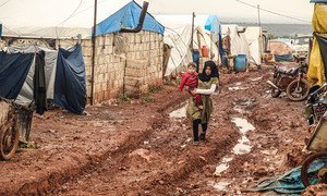A girl walks through the mud carrying her younger brother at the Khair Al-Sham IDP camp in Idlib Governorate, Syria.