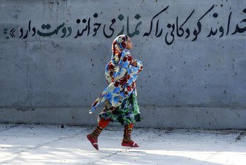 من الأرشيف: فتاة ترتدي حجابها في إيران تسير بقرب لوحة جدارية تقول باللغة الفارسية "إن الله يحب الأطفال الذين يصلون". 
