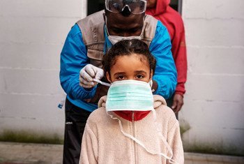 一名七岁的女孩在她居住的意大利罗马的非正式定居点接受健康检查前，被戴上一个口罩。