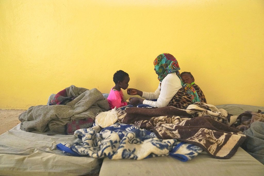 من الأرشيف: أم محتجزة مع طفليها أحدهما نائم على ظهرها والأخر يتناول الخبز من يدها في أحد مراكز الاحتجاز في بنغازي، ليبيا.