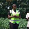 Kundi la watu, wakiwemo wanawake na wanaume, wamesimama katika shamba la mazao. Mwanamke mmoja amevaa fulana ya usalama ya njano, na mwingine ameshika chungwa.