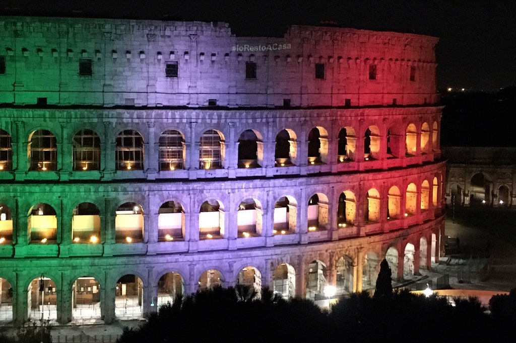 El Coliseo de Roma se ilumina por la noche con los colores de la bandera italiana, mostrando un mensaje que dice 'NoRestoACasa'.