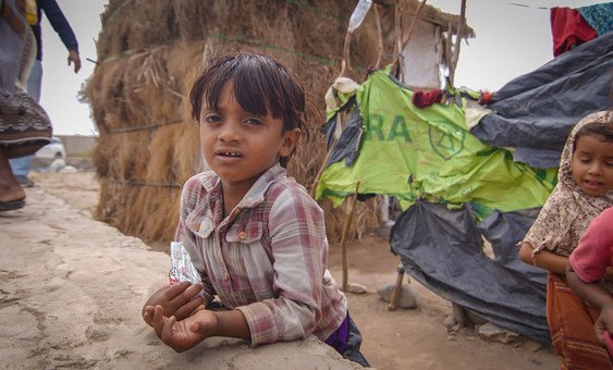 A young boy plays while his mother lines up at a water point in a camp for displaced people in Aden, southern Yemen.