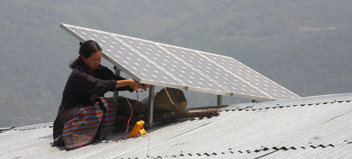 A woman installs a solar panel on a roof in Bhutan.