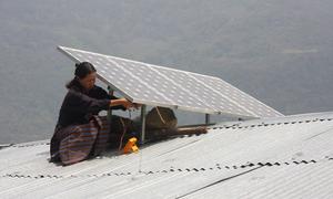 A woman installs a solar panel on a roof in Bhutan.