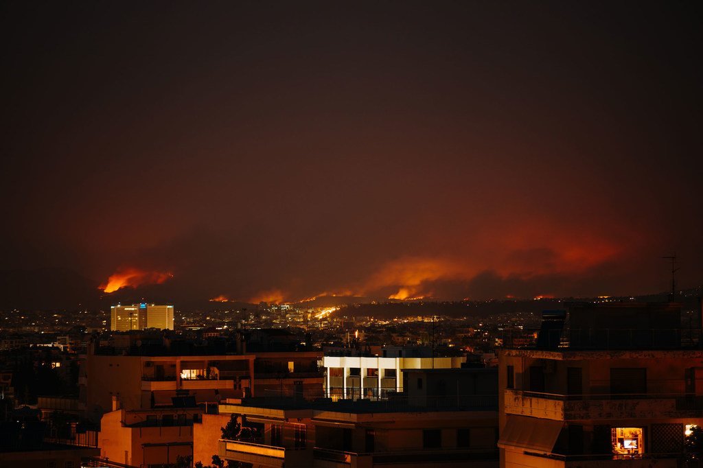 Vue nocturne d'Athènes, en Grèce, avec un important incendie de forêt qui fait rage sur les collines en arrière-plan, illuminant le ciel de flammes orangées et de fumée.