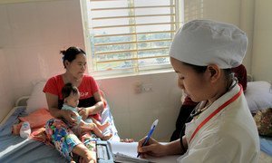 A woman and her child sit on a hospital bed in Makara, Cambodia, while a nurse reviews their medical charts. (file)