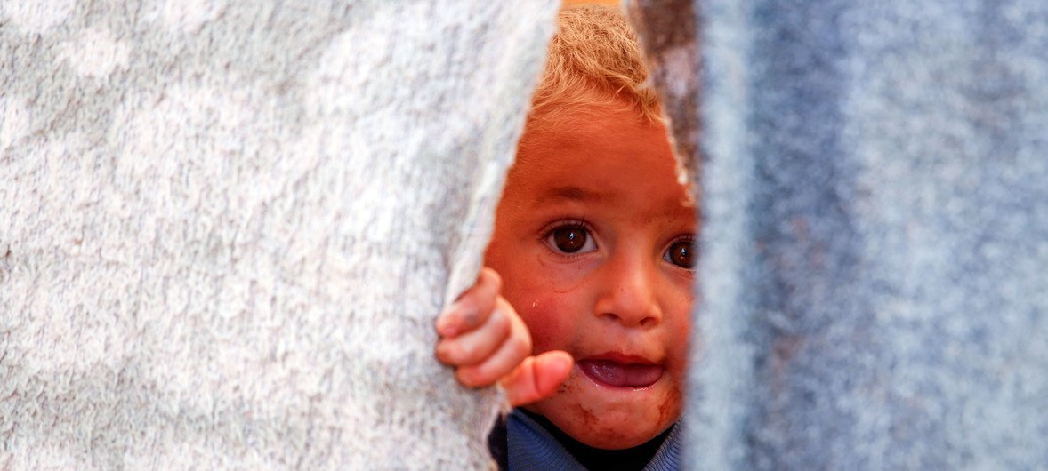 A Syrian child peeks out of a temporary shelter in an informal settlement in Killi, near the border with Turkey. (2019)