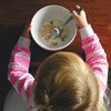 A little girl eats breakfast while sitting at a table.