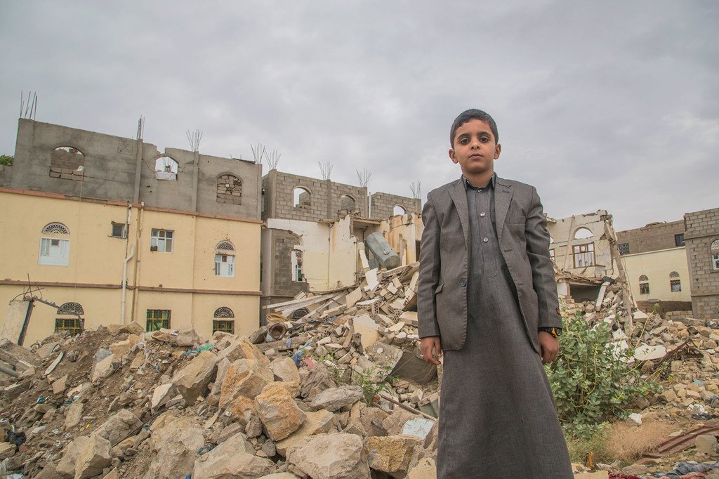 一名男孩站在也门萨达的一处受损建筑物前。