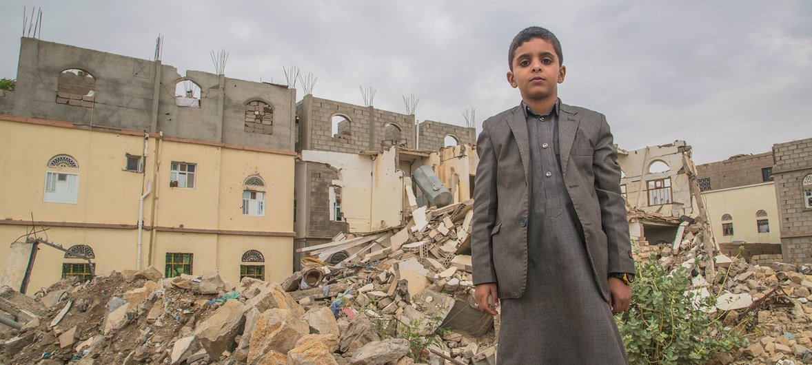 A young boy stands in front of damaged building in Saada, Yemen.
