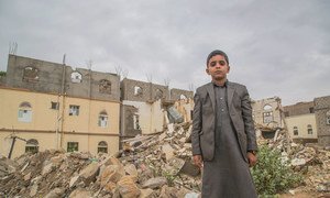 A young boy stands in front of damaged building in Saada, Yemen.