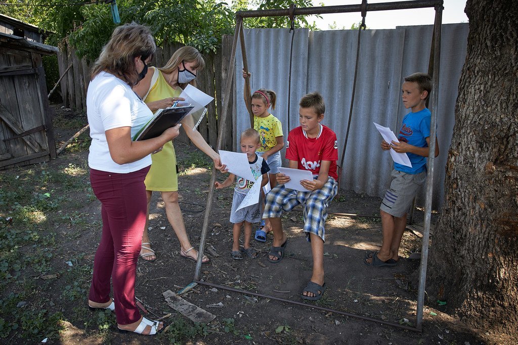 أخصائية اجتماعية (يسار) وخبيرة سيكولوجية (أقصى اليسار) تقدمان كراسات ألوان وكتبا للأطفال في شرقي أوكرانيا، خلال زيارة منزلية لأحد الأسر.