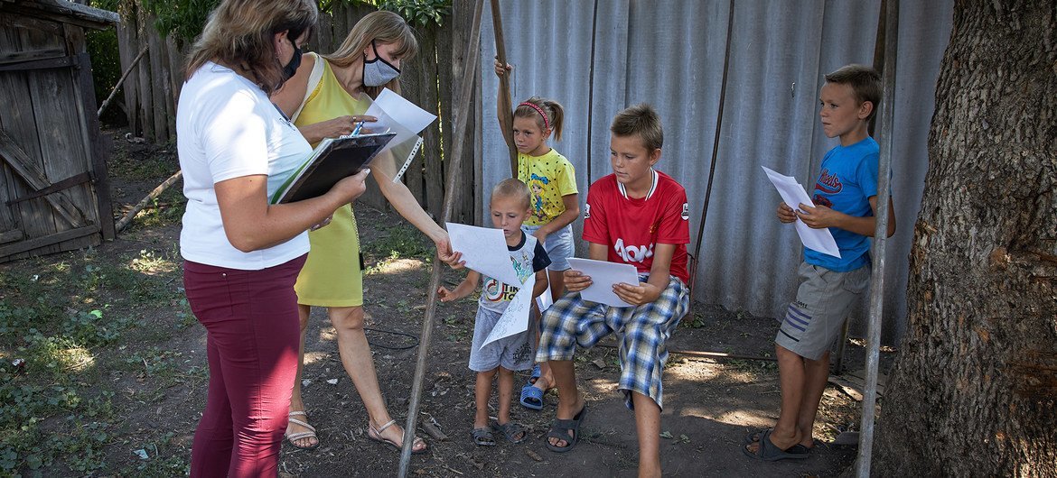 A social worker (left) and a psychologist (second from left) give colouring and exercise books to children in eastern Ukraine, during a home visit to meet with the family.