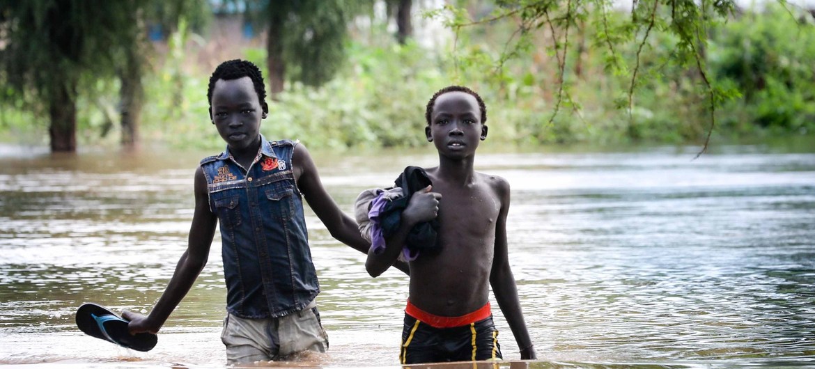 在埃塞俄比亚马班县的难民营中，两个男孩在没过膝盖的洪水中行走。