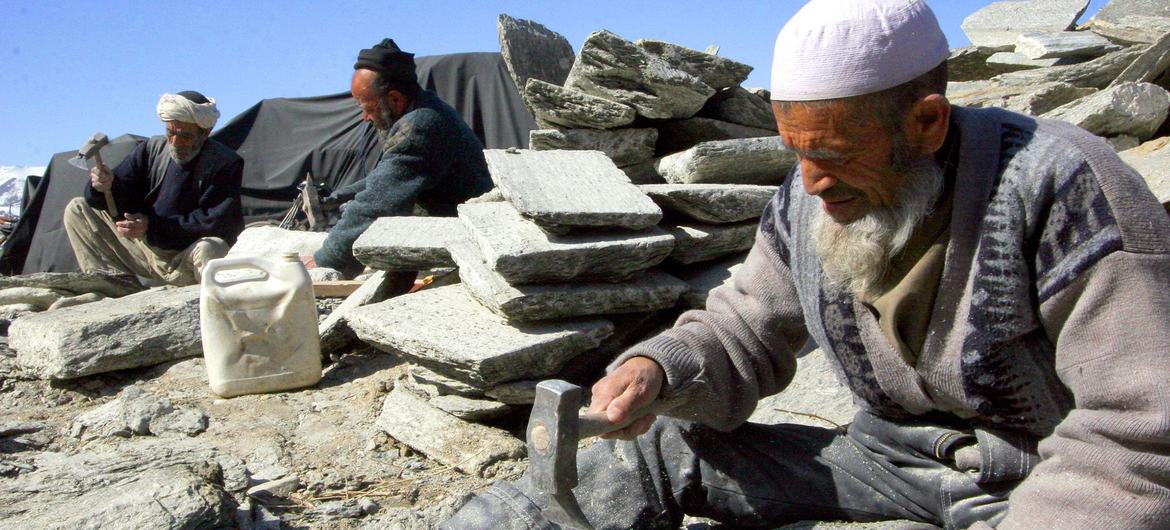 A group of Afghan men use hand tools to process rocks at a site in Kabul.