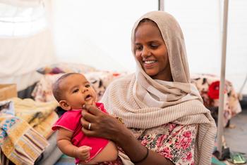 2022 年 8 月，一位母亲和她的孩子在苏丹东部的嗯拉库巴（ Um Rakuba） 难民营，与其他六名家庭成员和孩子一起住在一间小屋里。