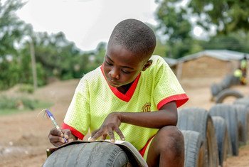घाना में एक बच्चा खुले स्थान में टायर को मेज़ बनाकर अपनी पढ़ाई करते हुए.