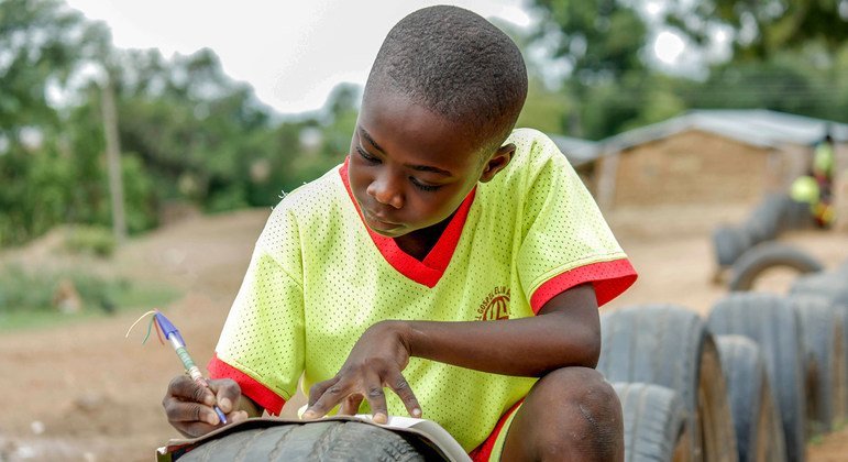 घाना में एक बच्चा खुले स्थान में टायर को मेज़ बनाकर अपनी पढ़ाई करते हुए.
