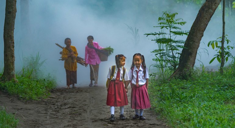 Two young schoolgirls walk through a forest in Indonesia.