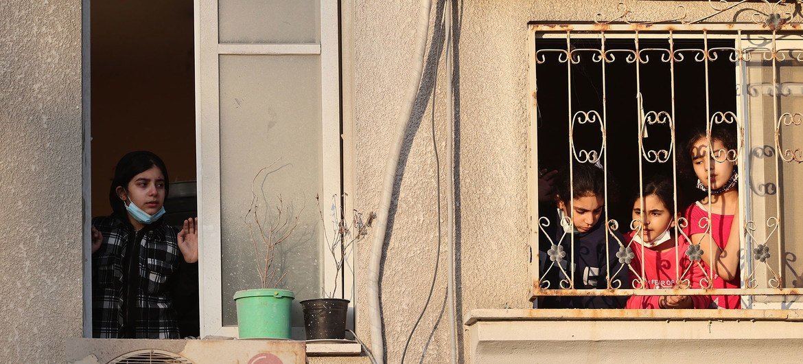 巴勒斯坦儿童从自家窗户向外望去，看着在加沙城附近被毁坏的建筑物。