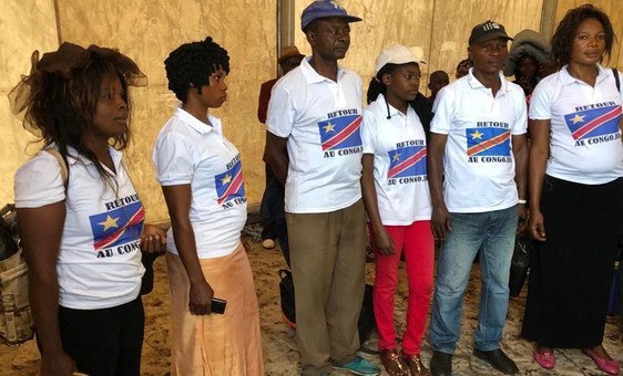 Um grupo de pessoas vestindo camisetas com a bandeira da República Democrática do Congo e a inscrição 'RETOUR AU CONGO', representando refugiados da RDC que retornam ao país.