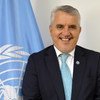Adoniran Sanches sorri durante um retrato oficial com a bandeira da FAO ao fundo.