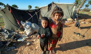 叙利亚霍姆斯南部偏远农村地区的一个营地，孩子们站在帐篷外，周围都是沙地。