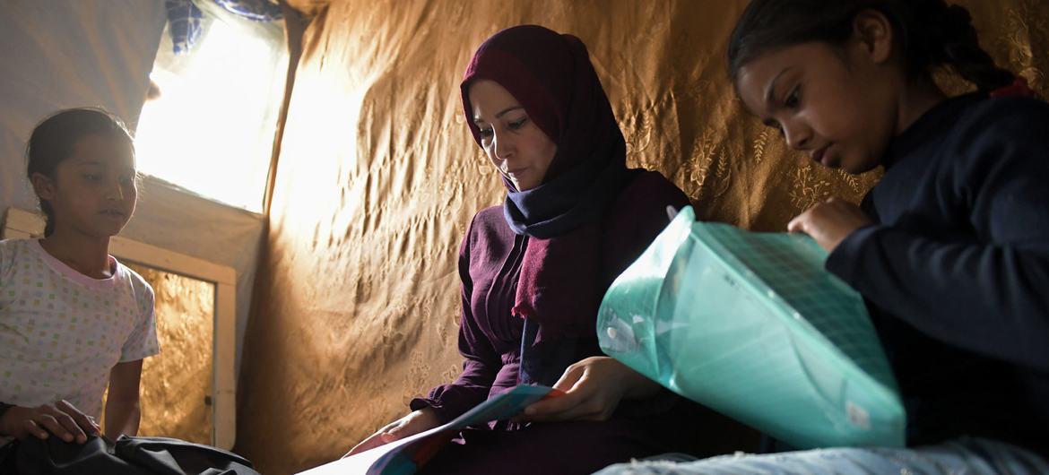 اللاجئة السورية والأرملة ماجدة شحادة ابراهيم، هي أم لأربعة أطفال، وفي الصورة تقوم بمساعدة بناتها في دراستهم في مخيم عسكر بلبنان.
