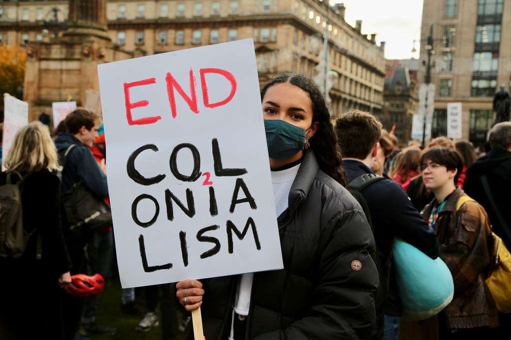 A young activist attends a climate action rally in Glasgow, Scotland, holding a banner calling for an end to colonialism.