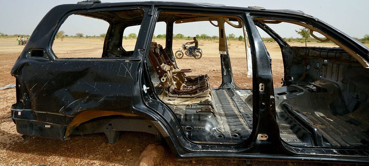 رجل يقود دراجة نارية بجانب سيارة محترقة في المنطقة الشمالية من بوركينا فاسو حيث تستمر الحوادث الأمنية في الارتفاع. (يونيو 2019)