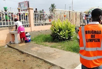 Un homme portant un gilet orange de la "brigade de nettoyage" regarde une femme se laver les mains sur un marché de Luanda, Angola