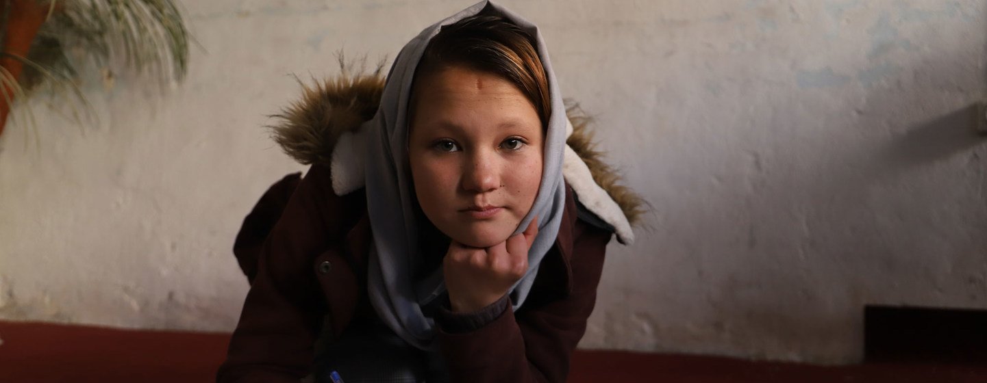 Une jeune fille, Zainab, écrit dans un cahier tout en regardant l'appareil photo.