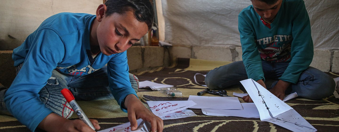 Dos niños fabrican mascarillas de papel en un campamento de refugiados en Siria.